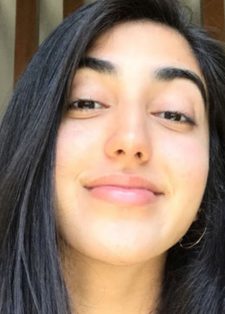 A young woman with long dark hair smiles subtly while looking at the camera
