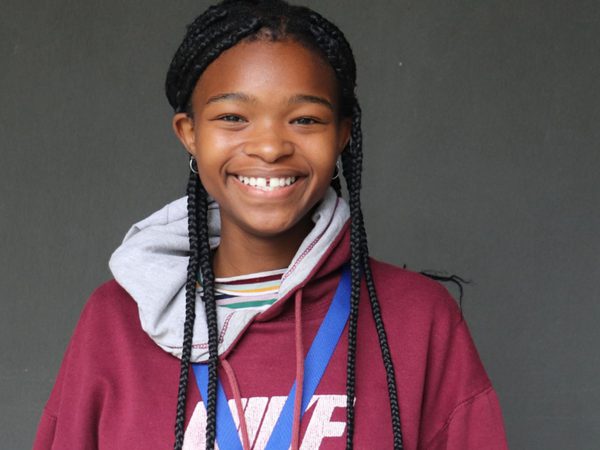 Smiling girl with braided hair wearing a maroon hoodie and blue lanyard