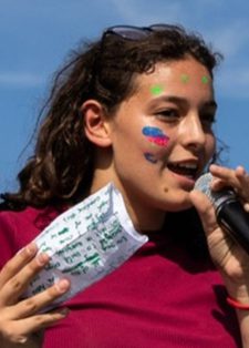 A young woman with face paint speaks into a microphone