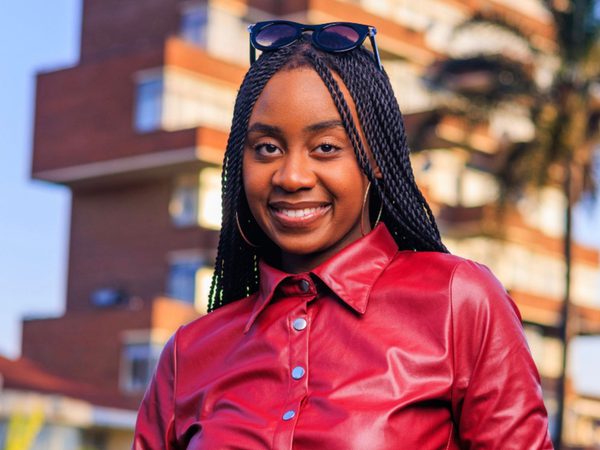 Young woman with braided hair and sunglasses on head, wearing a red leather jacket, smiles confidently