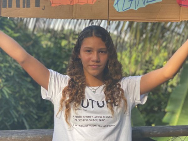 A young woman stands outside, holding a handmade cardboard sign with colourful drawings
