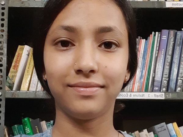 A person with dark hair smiles softly in front of bookshelves