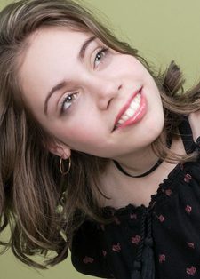 Smiling young woman with wavy brown hair, tilting her head against a green background