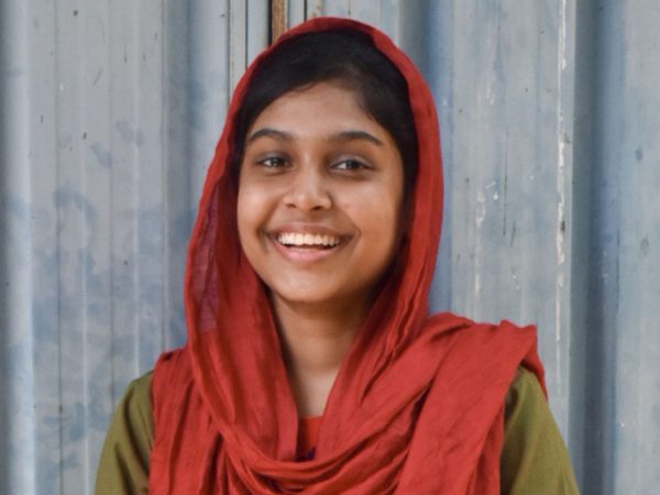 Smiling young woman in a red headscarf stands against a textured grey metal background
