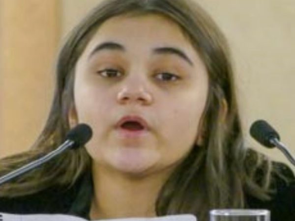 A young person sits between two microphones, speaking with a focused expression