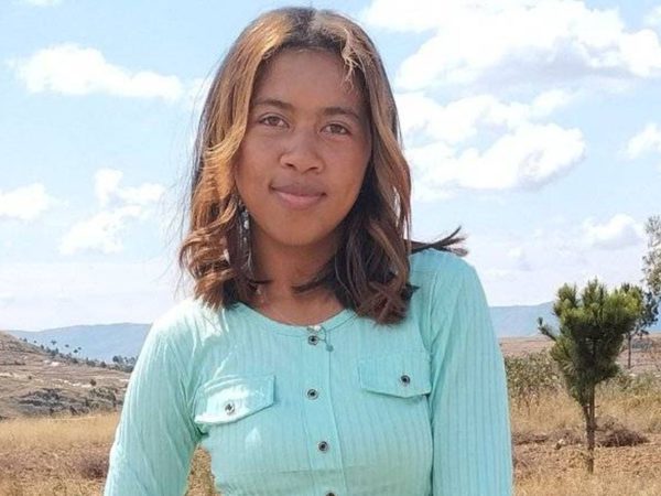 Young woman in a light green shirt stands in a grassy field with scattered trees