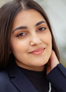 Smiling woman with long brown hair wearing a navy blazer and black top
