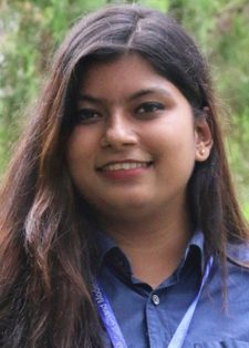 Saiban Binte Shahaj looks into the camera with trees behind her. She has long brown hair and is wearing a blue shirt and lanyard.