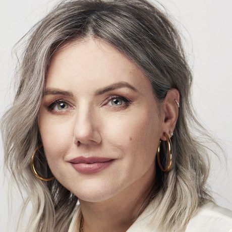 Headshot of Sali Hughes, who has shoulder length, wavy blonde hair and is wearing a pair of hold hooped earrings and a light coloured top.