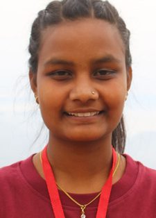 Saru Khadka looks into the camera smiling. She has long brown hair tied up in a pony tail, and is wearing a red top and lanyard.