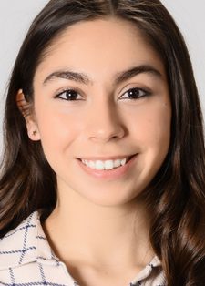 Headshot of Selin Özünaldım smiling in the camera. She has long brown hair and is wearing a cream and blue check top.