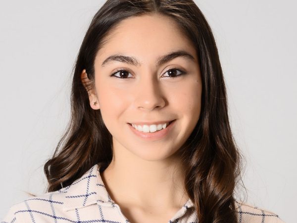 Headshot of Selin Özünaldım smiling in the camera. She has long brown hair and is wearing a cream and blue check top.
