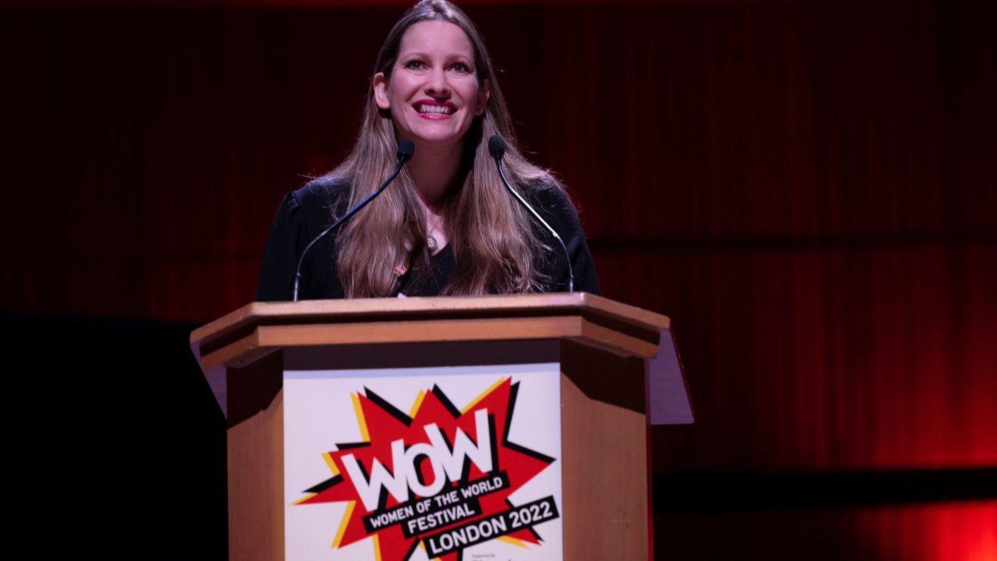The author Laura Bates stands at a lectern at the WOW Festival