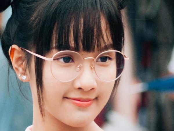 A young person with round glasses and a small smile stands outdoors