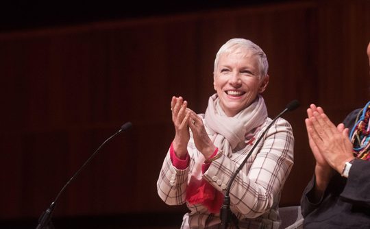 Two women sit on stage clapping