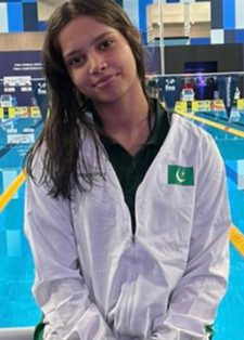 Young woman in a white jacket smiling softly by an indoor swimming pool