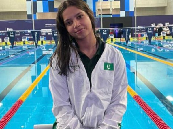 Young woman in a white jacket smiling softly by an indoor swimming pool