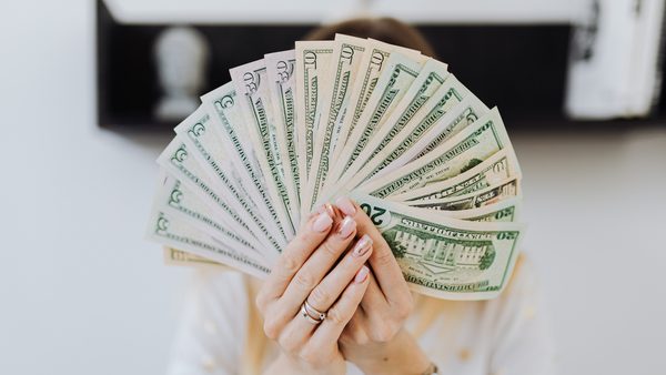 A woman holds dollar bills fanned out in front of her face