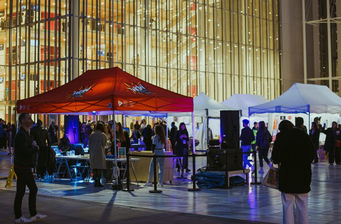 A night market scene features a red tent with people gathered underneath, set against an illuminated building backdrop.