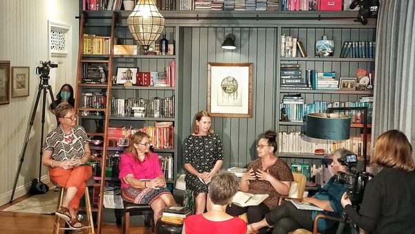 Cozy library room with bookshelves filled with books and decor. Seven people sit in discussion, creating an engaged, warm, and collaborative atmosphere.