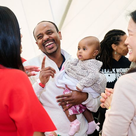 A joyful group of diverse adults and a baby share a lighthearted moment, smiling and interacting warmly
