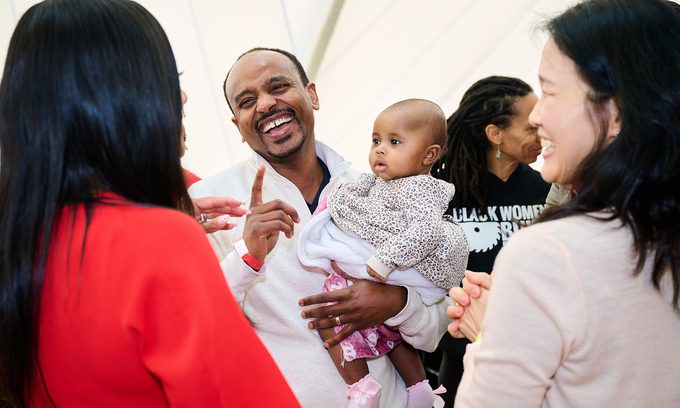 A joyful group of diverse adults and a baby share a lighthearted moment, smiling and interacting warmly