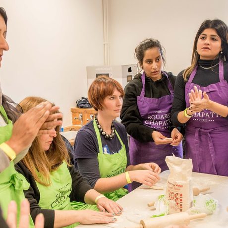 A group of women in aprons gather around a table, engaged in a cooking class, focusing on dough-making