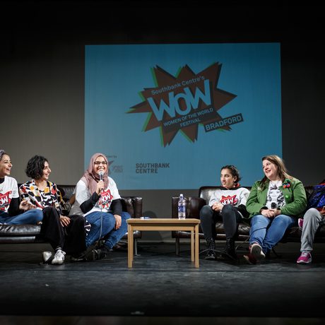 A panel of six people sits on a stage in discussion with "WoW" logo projected behind them.