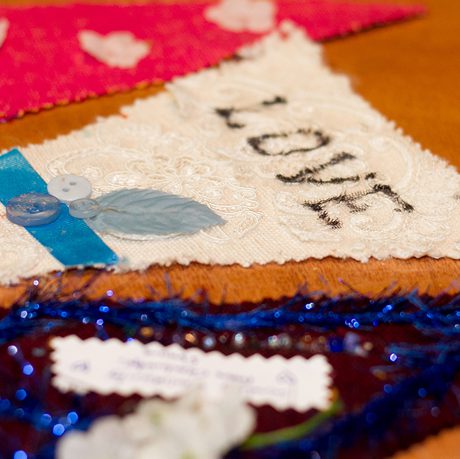 Fabric triangles with various textures and colours are laid out. A white triangle is in the centre, decorated with blue leaves and the word "LOVE".