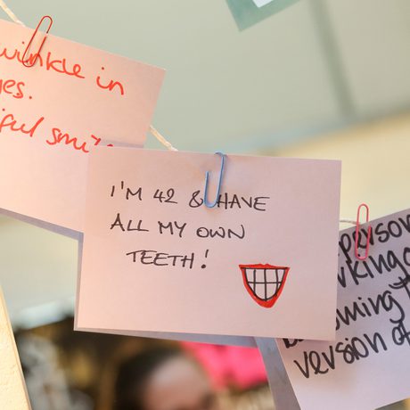 Notes with positive affirmations are attached to a string. Messages include "The twinkle in my eyes" and "I'm 42 and have all my own teeth!"