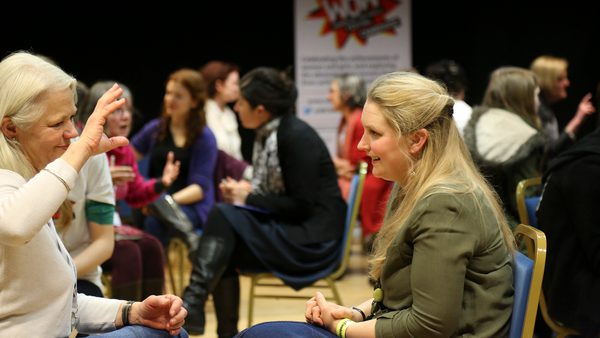 Women engage in conversations seated in pairs at a workshop. The room is lively