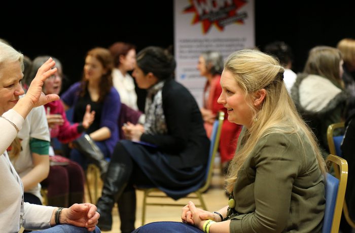 Women engage in conversations seated in pairs at a workshop. The room is lively