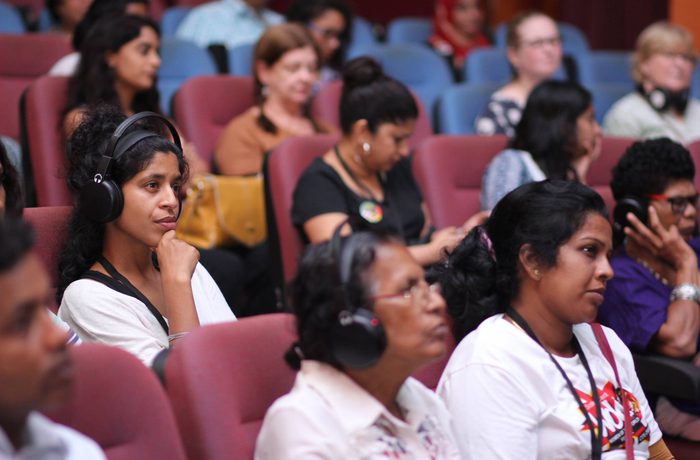 Audience members seated in rows at a conference, wearing headphones.