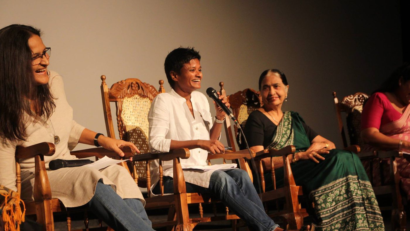 A panel of four women seated in ornate chairs on a stage, engaged in discussion. The atmosphere is lively, with smiles and casual attire.