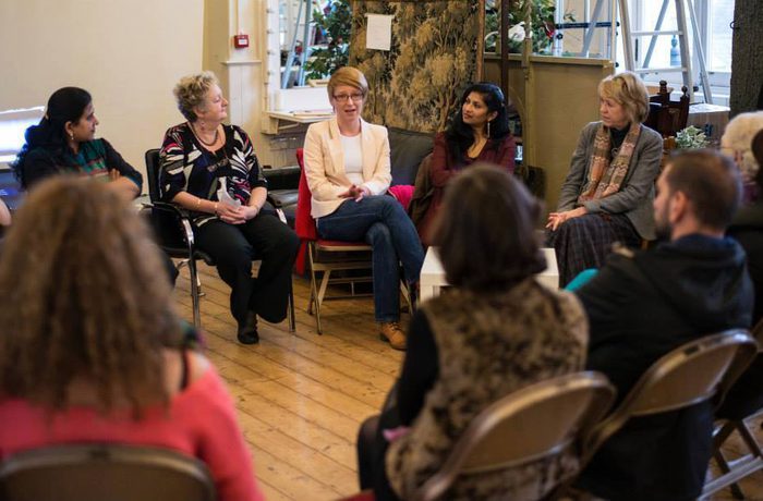 A diverse group of people sit in a circle on chairs in a cozy room, engaged in a focused discussion. The atmosphere is warm and collaborative.