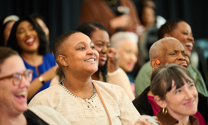 A diverse group of people seated indoors, smiling and laughing. The mood is joyful and lively
