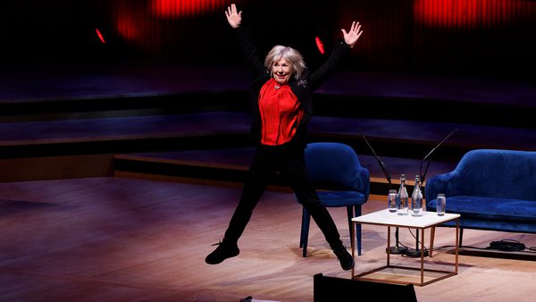 A person in a red shirt joyfully jumps on a stage with a broad smile.