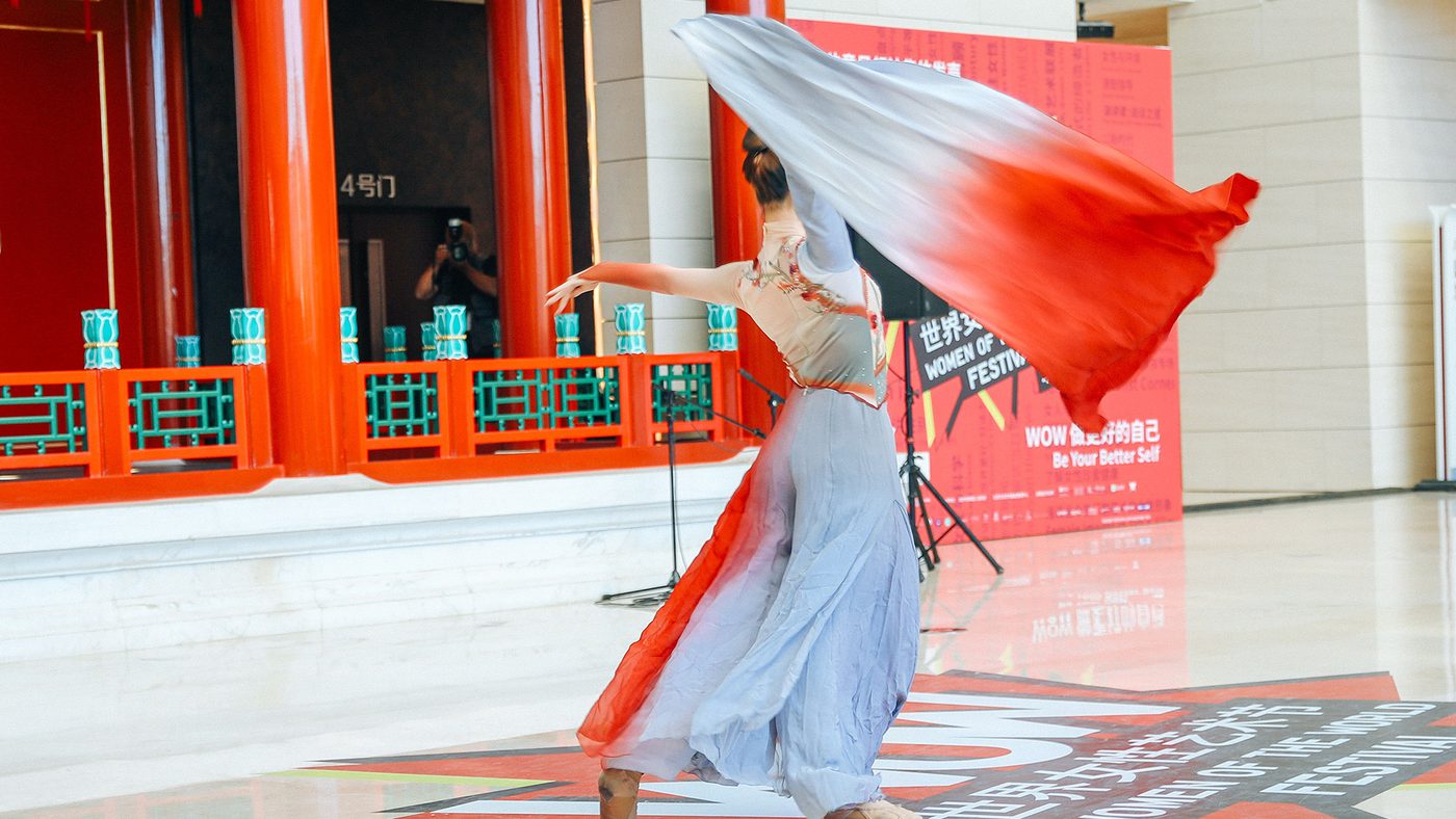 A dancer twirls gracefully in a flowing red and white dress, set against vibrant red columns