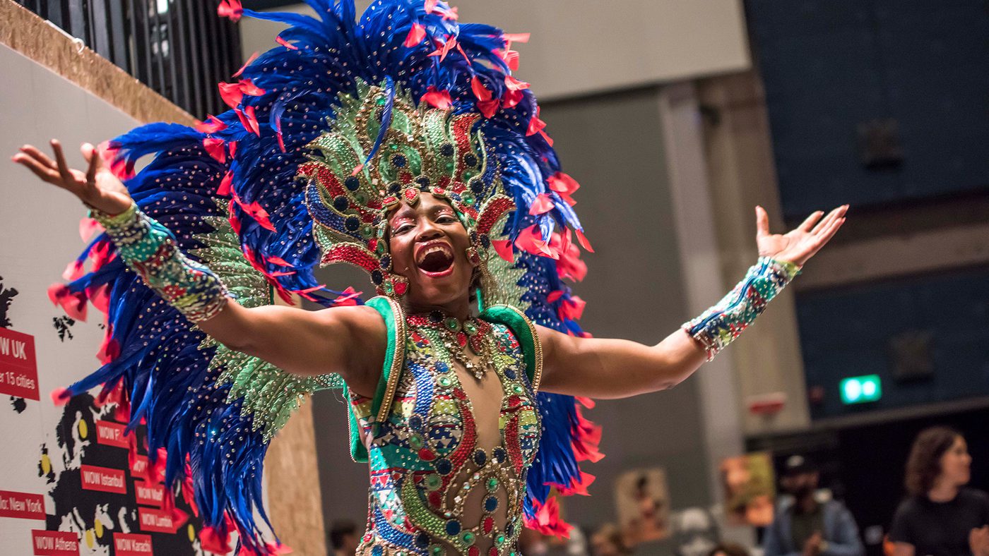 Dancer in vibrant, feathered costume joyfully performs with outstretched arms and smile